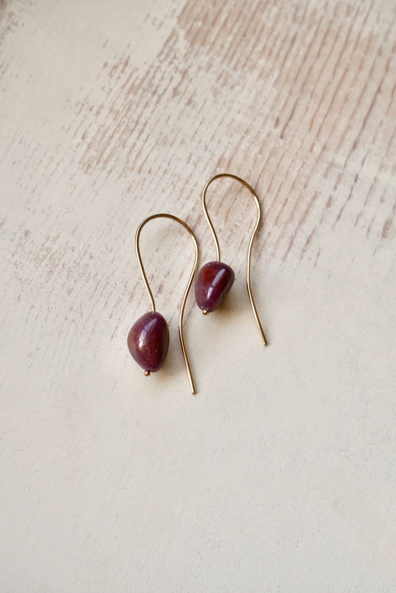 May include: A pair of gold dangle earrings with a deep purple gemstone on each earring.