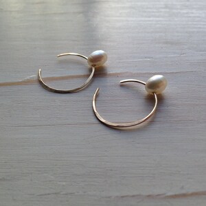 May include: A pair of gold hoop earrings with a single white pearl on each hoop.
