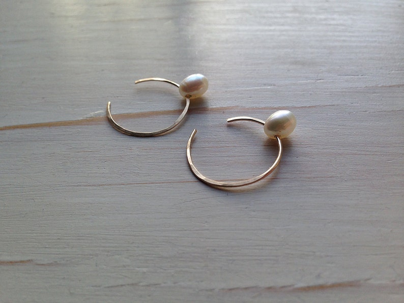 May include: A pair of gold hoop earrings with a single white pearl on each hoop.