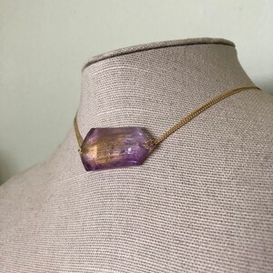 May include: A gold chain necklace with a large, faceted, purple gemstone pendant.