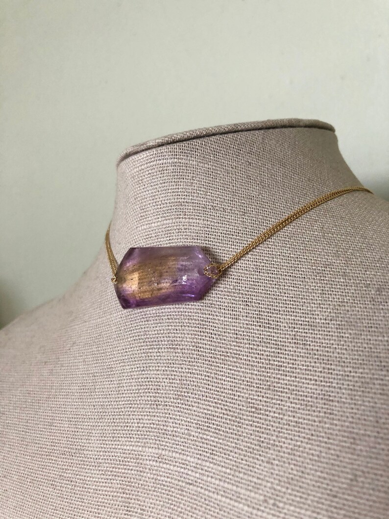 May include: A gold chain necklace with a large, faceted, purple gemstone pendant.