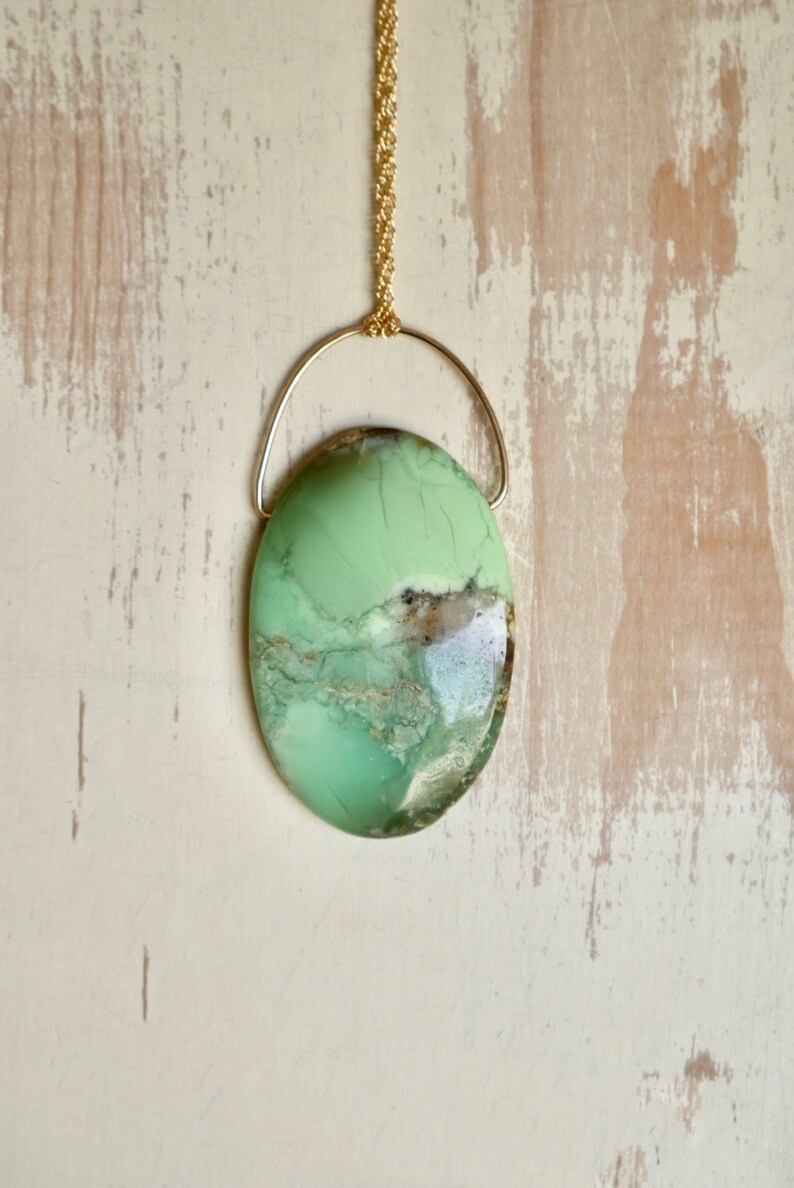 Puede incluir: Un collar con un colgante ovalado verde y marr&oacute;n, una cadena de oro y un bucle de alambre dorado.