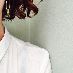 May include: A pair of gold hoop earrings with a small green gemstone dangling from the bottom.