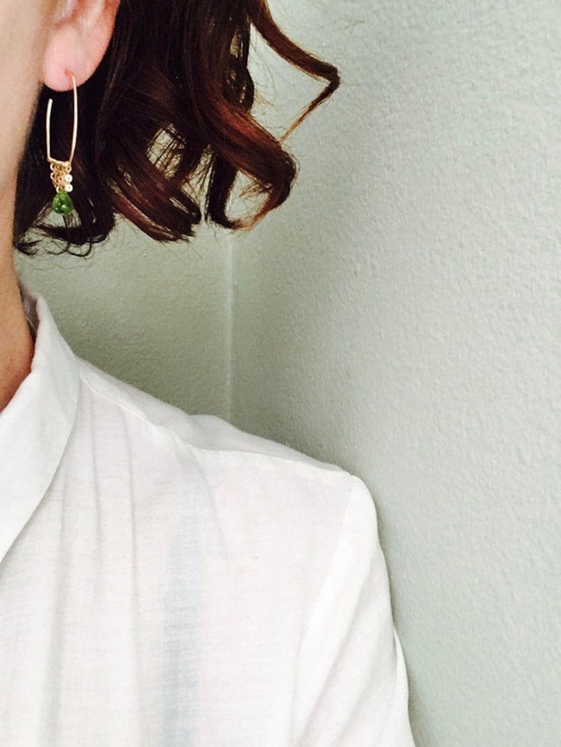 May include: A pair of gold hoop earrings with a small green gemstone dangling from the bottom.