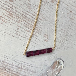 May include: A gold chain necklace with a bar of purple gemstones.