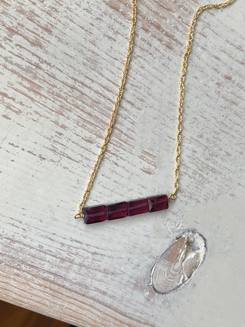 May include: A gold chain necklace with a bar of purple gemstones.