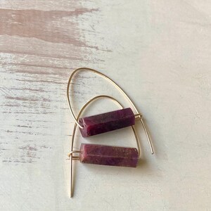 May include: A pair of gold hoop earrings with a rectangular purple stone hanging from each hoop.