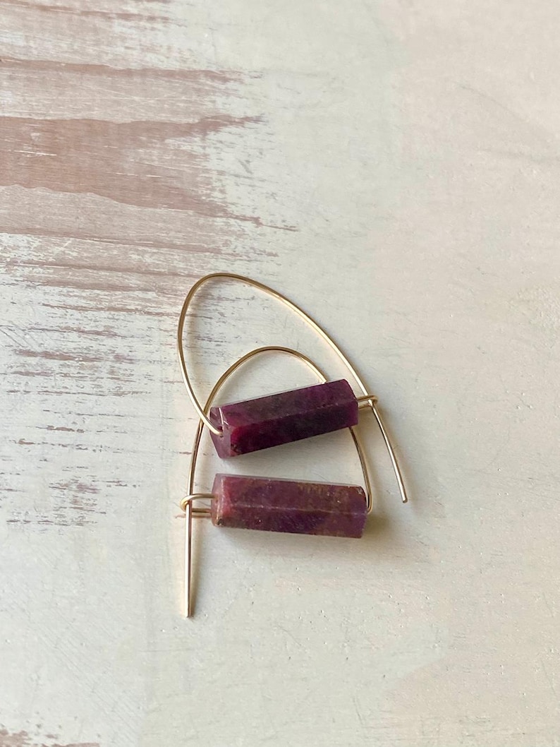 May include: A pair of gold hoop earrings with a rectangular purple stone hanging from each hoop.