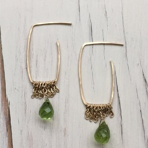 May include: Gold hoop earrings with a delicate chain fringe and a green gemstone drop.