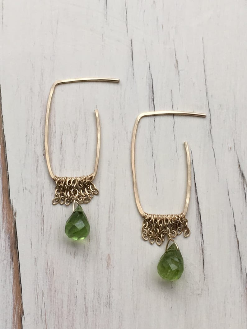 May include: Gold hoop earrings with a delicate chain fringe and a green gemstone drop.