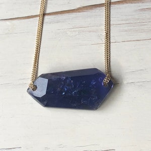 May include: A gold chain necklace with a large, faceted, dark blue gemstone pendant.