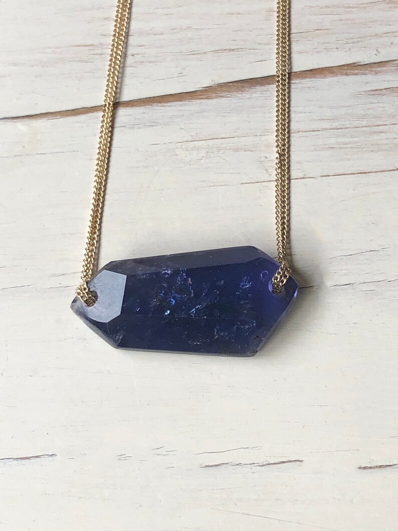 May include: A gold chain necklace with a large, faceted, dark blue gemstone pendant.