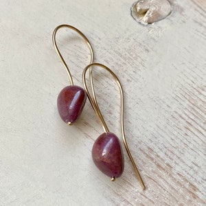 May include: A pair of gold dangle earrings with a deep purple stone on each earring.