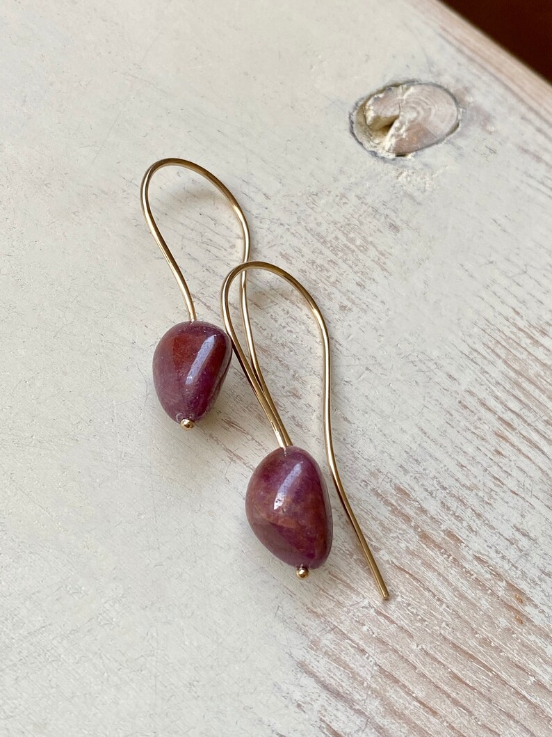 May include: A pair of gold dangle earrings with a deep purple stone on each earring.