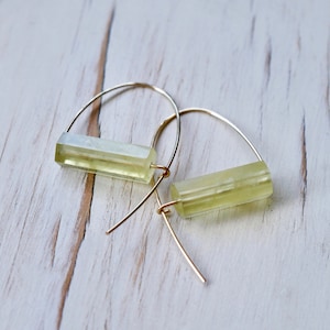 May include: A pair of gold hoop earrings with a light green rectangular stone hanging from each hoop.