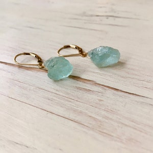 Peut inclure: Une paire de boucles d'oreilles en or avec des pierres de cristal d'aigue-marine bleu clair. Les pierres sont brutes et ont une forme irr&eacute;guli&egrave;re naturelle.