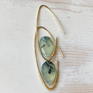 May include: Gold wire earrings with green and black gemstone drops. The earrings are made with a simple wire loop design.