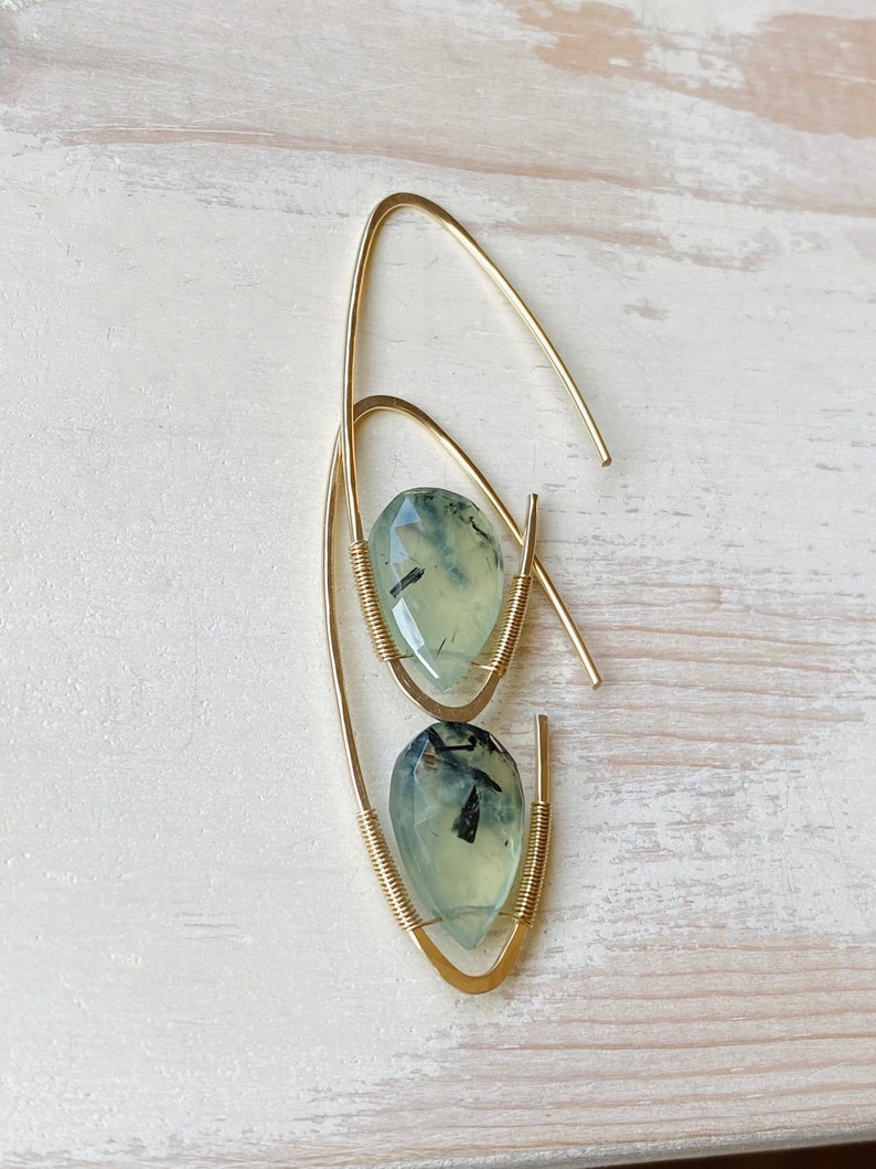 May include: Gold wire earrings with green and black gemstone drops. The earrings are made with a simple wire loop design.