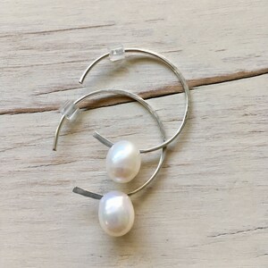 May include: A pair of silver hoop earrings with a white pearl dangling from each hoop.