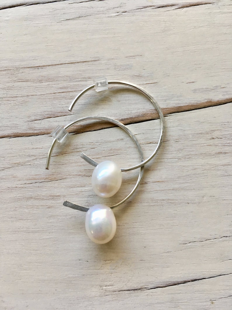 May include: A pair of silver hoop earrings with a white pearl dangling from each hoop.
