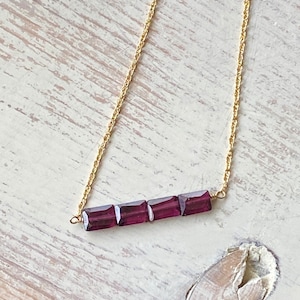 May include: A gold chain necklace with a bar of four square-shaped purple gemstones.
