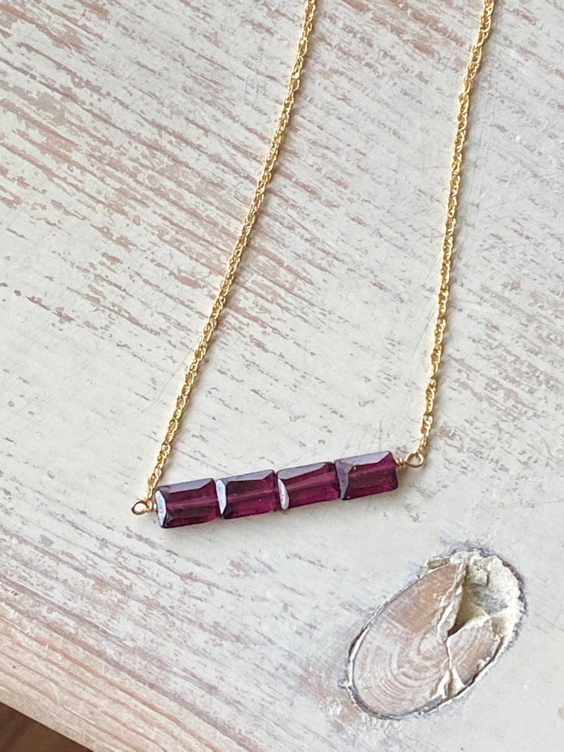 May include: A gold chain necklace with a bar of four square-shaped purple gemstones.