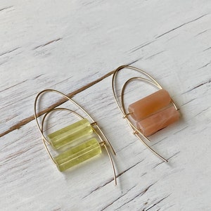 May include: A pair of gold hoop earrings with a stacked rectangular stone. One earring has a light green stone and the other has a light peach stone.