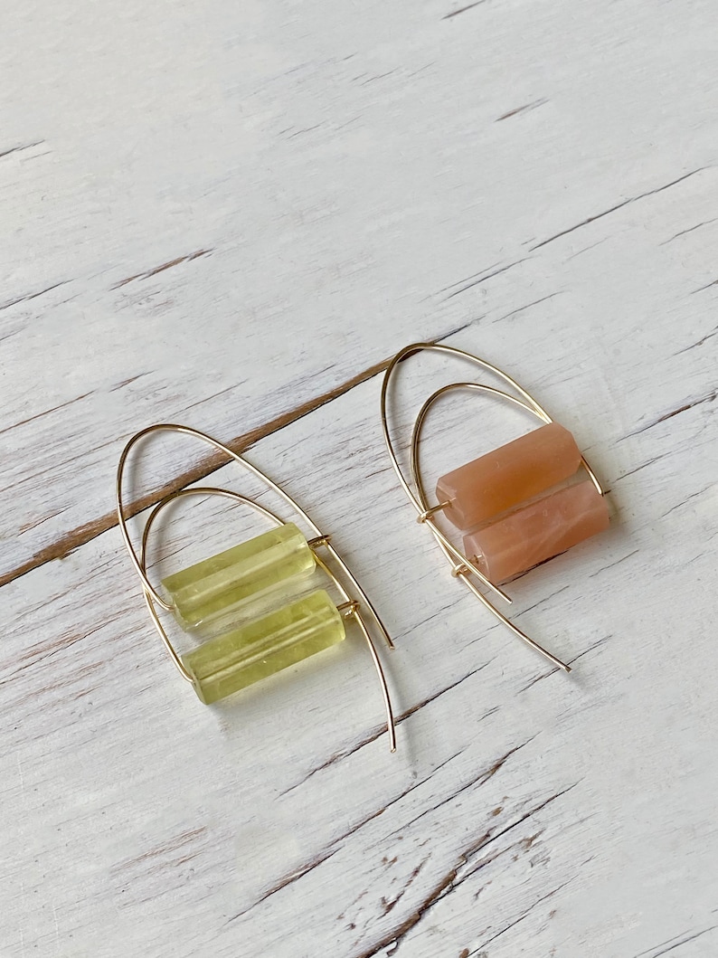 May include: A pair of gold hoop earrings with a stacked rectangular stone. One earring has a light green stone and the other has a light peach stone.