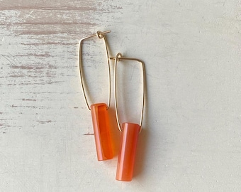 Könnte beinhalten: Ein Paar goldene Creolen mit orangefarbenen Edelstein-Anhängern. Die Creolen sind rechteckig und die Edelsteine sind zylindrisch.