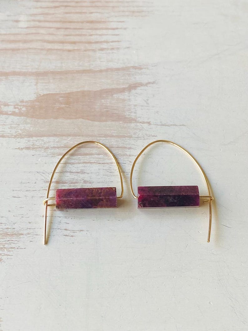 May include: A pair of gold hoop earrings with a rectangular purple stone pendant. The earrings are simple and elegant.