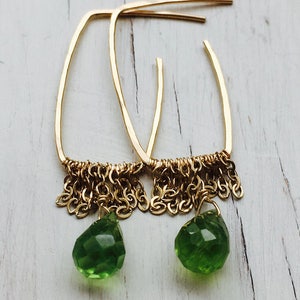 May include: Gold hoop earrings with a dangling chain and a green gemstone drop.