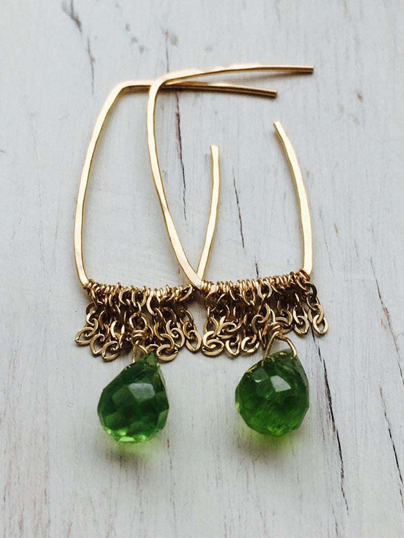 May include: Gold hoop earrings with a dangling chain and a green gemstone drop.