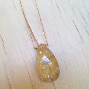 May include: A gold chain necklace with a teardrop-shaped, clear yellow crystal pendant.