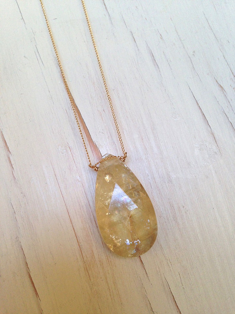 May include: A gold chain necklace with a teardrop-shaped, clear yellow crystal pendant.
