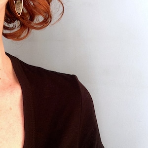 May include: A woman with red hair wearing a black v-neck shirt and a gold hoop earring with a clear stone.
