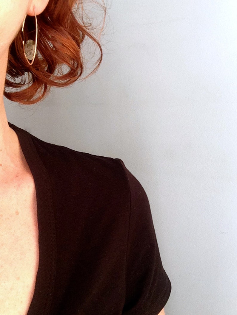 May include: A woman with red hair wearing a black v-neck shirt and a gold hoop earring with a clear stone.
