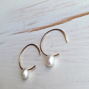 May include: A pair of gold hoop earrings with a single white pearl dangling from each hoop.