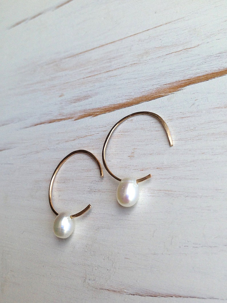 May include: A pair of gold hoop earrings with a single white pearl dangling from each hoop.