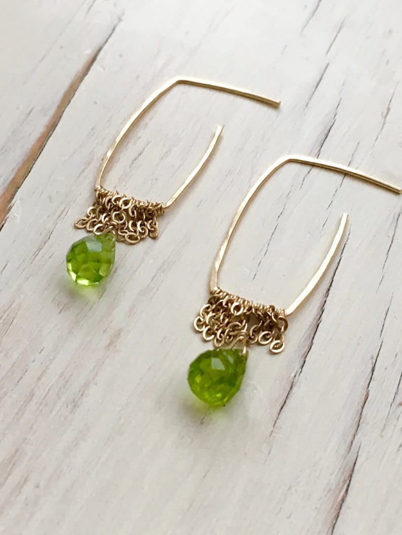 May include: Gold earrings with a teardrop shaped green peridot stone and a dangling chain of gold beads.