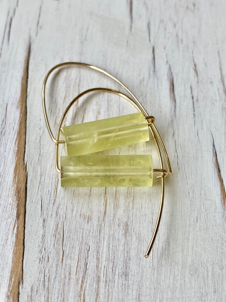 May include: Gold hoop earrings with a light yellow rectangular stone. The stone has a translucent, slightly cloudy appearance.
