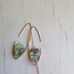 May include: A pair of gold earrings with green and black gemstone drops. The earrings are made with thin wire and have a simple, elegant design.