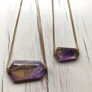 May include: Two gold chain necklaces with amethyst and citrine crystal pendants. The pendants are faceted and have a purple and yellow color gradient.