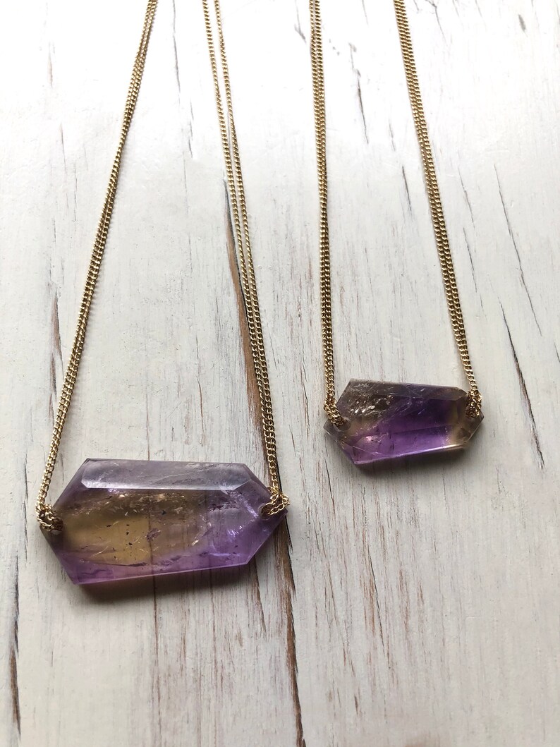 May include: Two gold chain necklaces with amethyst and citrine crystal pendants. The pendants are faceted and have a purple and yellow color gradient.