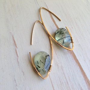 May include: A pair of gold earrings with green and black gemstone drops. The earrings are made with thin, curved wire.