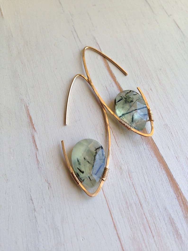 May include: A pair of gold earrings with green and black gemstone drops. The earrings are made with thin, curved wire.