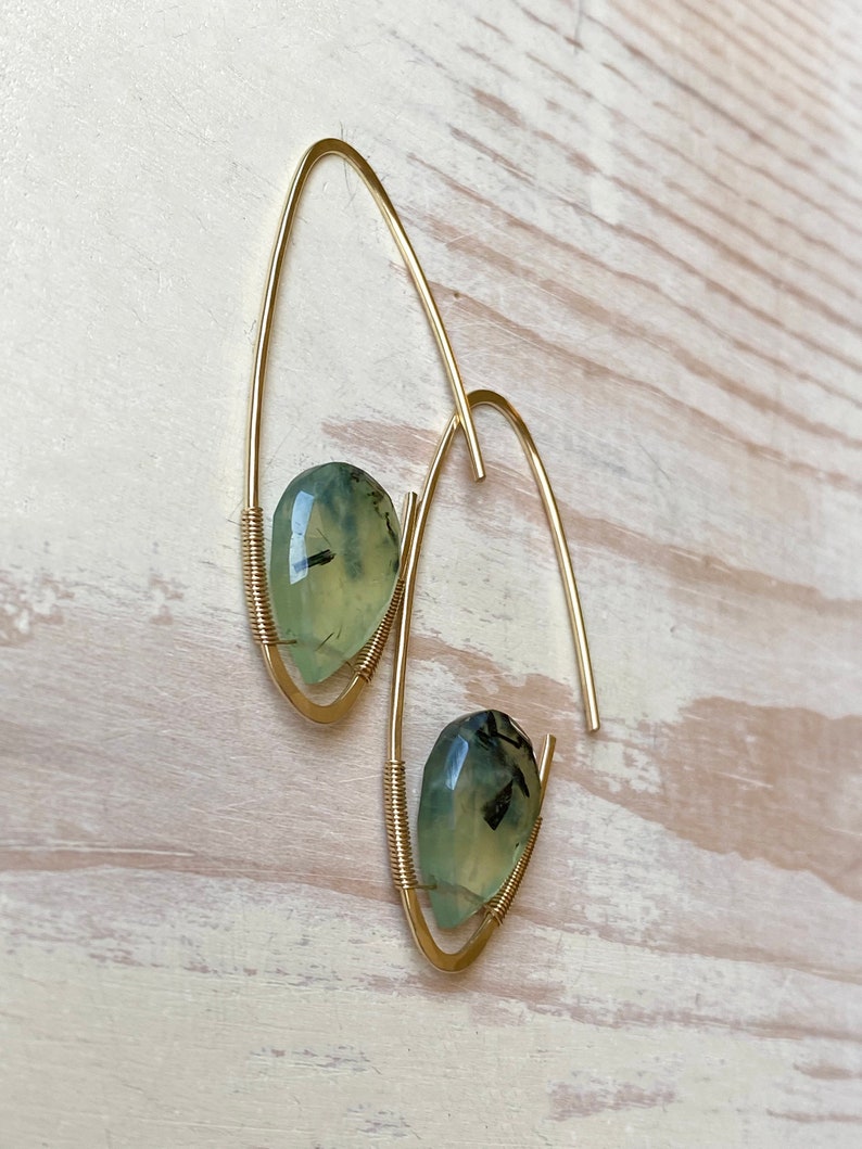 May include: Gold hoop earrings with green and black gemstone accents.