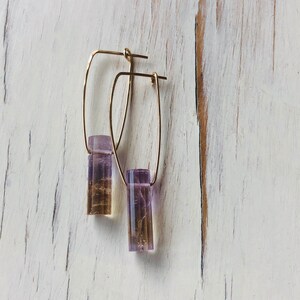 May include: A pair of gold hoop earrings with a purple and brown rectangular stone pendant hanging from each hoop.