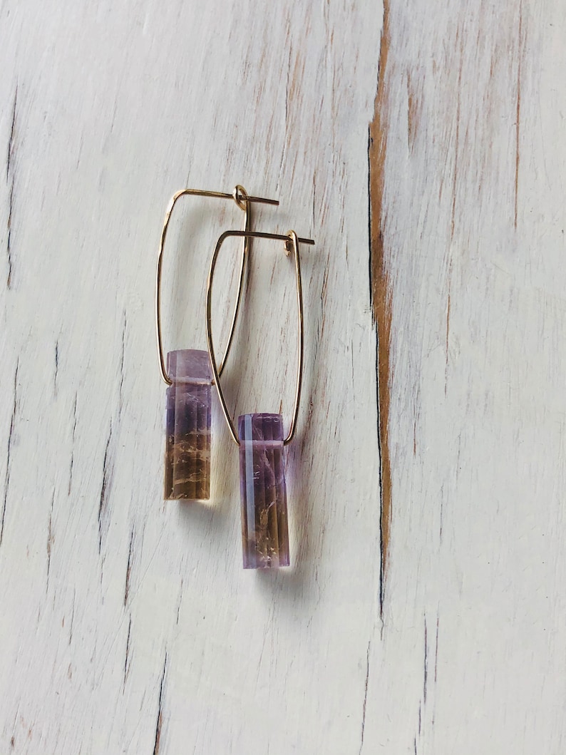 May include: A pair of gold hoop earrings with a purple and brown rectangular stone pendant hanging from each hoop.