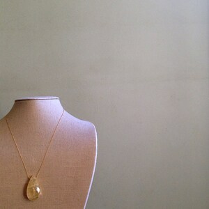 May include: A gold chain necklace with a teardrop-shaped pendant made of clear, yellow-tinted glass. The necklace is displayed on a fabric-covered mannequin bust.