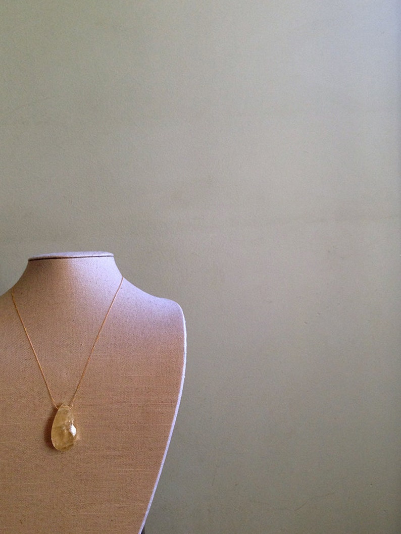 May include: A gold chain necklace with a teardrop-shaped pendant made of clear, yellow-tinted glass. The necklace is displayed on a fabric-covered mannequin bust.